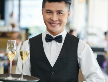 Image of waiter smiling and holding a tray of champagne for Learn Q blog on catering and hospitality FAQs