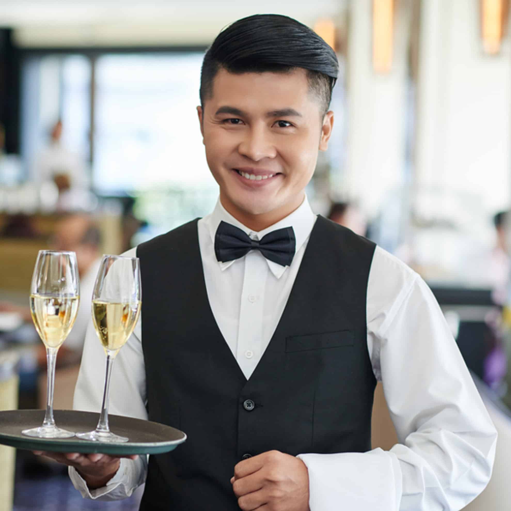 Image of waiter smiling and holding a tray of champagne for Learn Q blog on catering and hospitality FAQs